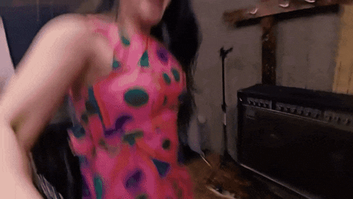 a woman in a pink dress is dancing in front of a black amplifier