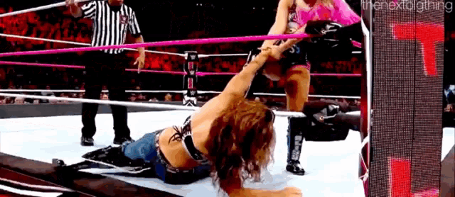 a woman is laying on the ground in a wrestling ring while a referee looks on .