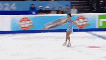 a girl in a blue dress is ice skating in front of a wall that has the number 24 on it