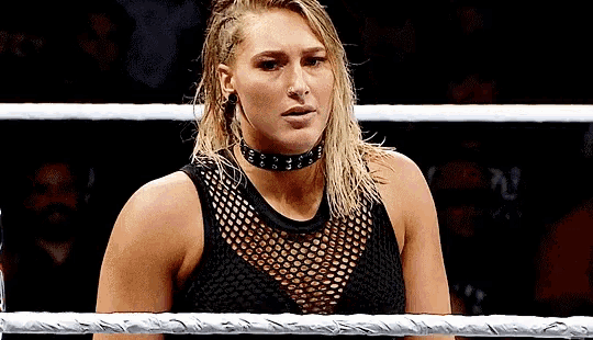a woman is standing in a wrestling ring wearing a choker and a black tank top