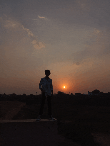 a silhouette of a person standing in front of a sunset sky