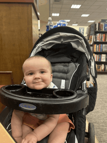a baby is sitting in a graco stroller and smiling