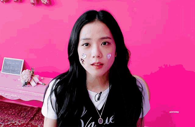 a girl with stickers on her face stands in front of a pink wall with a sign that says welcome