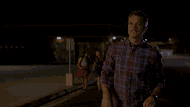 a man in a plaid shirt is standing in front of a sign that says i need to meet your grandmother