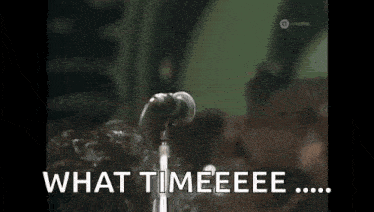 a man with curly hair singing into a microphone with the words what timeeeee written below him .
