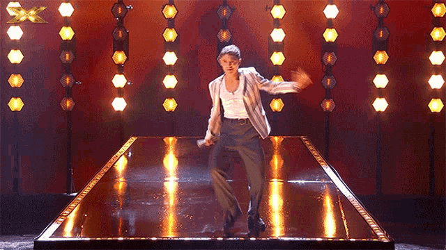 a man in a suit is dancing on a stage with an x on the bottom right