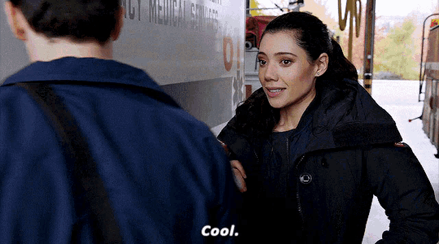 a woman in a black jacket is standing next to a man in a blue jacket and saying cool