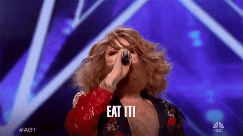 a man with a beard is singing into a microphone and says eat it !