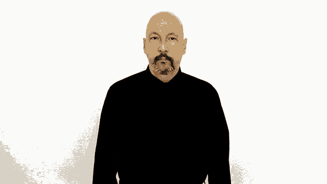 a bald man with a beard and mustache is wearing a black shirt and making a gesture with his hands .