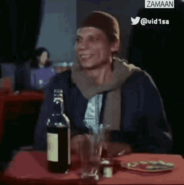 a man is sitting at a table with a bottle of liquor and a glass of beer .