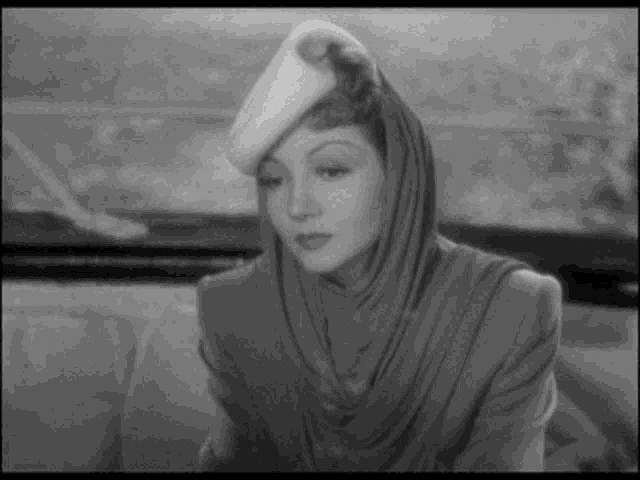 a black and white photo of a woman wearing a hat and a scarf .