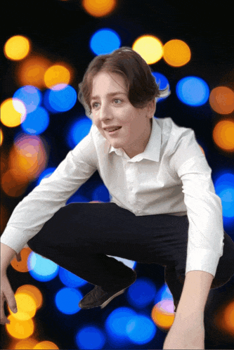 a boy in a white shirt and black pants is squatting in front of a blurry background