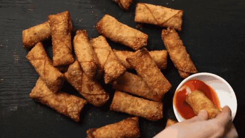 a person dipping a fried egg roll in a bowl of sauce