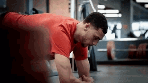 a man in a red shirt is doing a plank exercise in a gym .