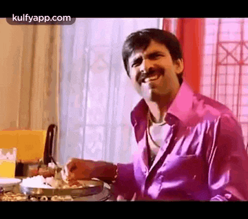 a man in a pink shirt is sitting at a table with a bowl of food .