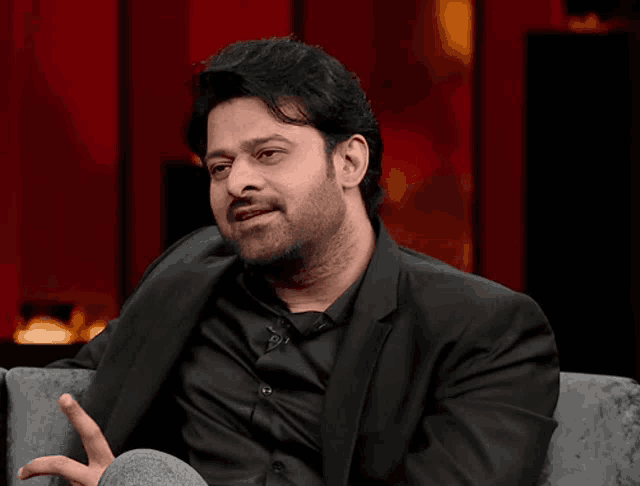 a man in a suit and black shirt is sitting in a chair and talking