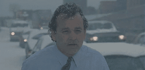 a man in a suit and tie is standing in the snow and talking about blizzards .