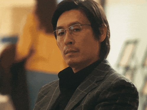 a man wearing glasses and a suit looks serious