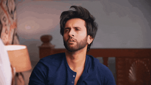 a man with a beard wearing a blue shirt making a funny face