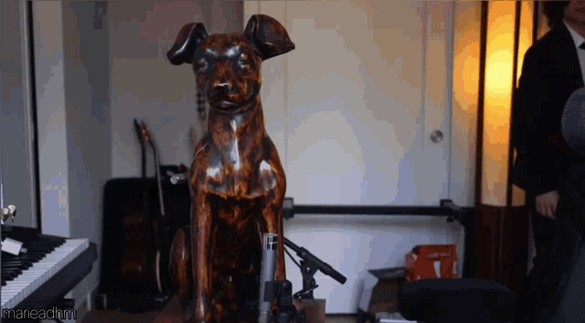 a statue of a dog sits in front of a microphone in a room with a man standing behind it