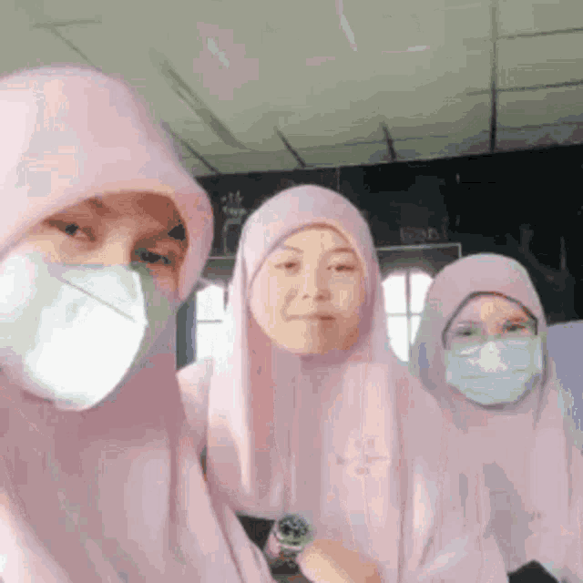 three women wearing hijabs and face masks are posing for a picture together .
