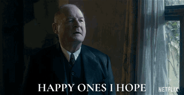 a man in a suit and tie says " happy ones i hope " in front of a window