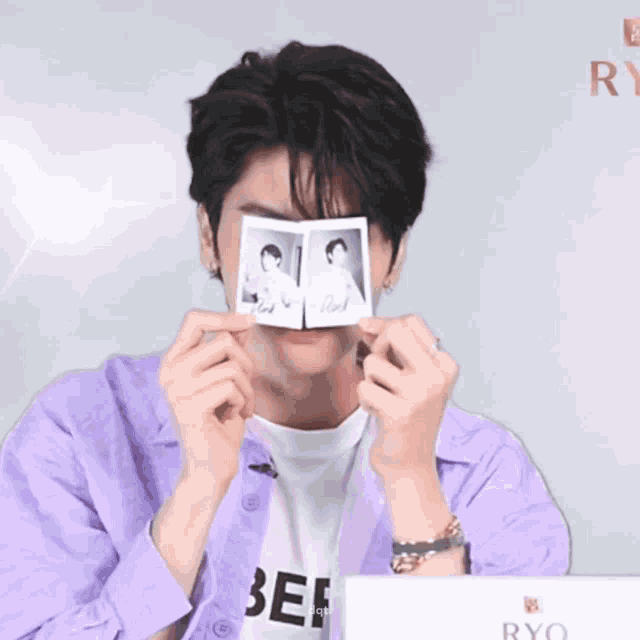 a young man in a purple shirt is holding up two polaroid pictures and smiling