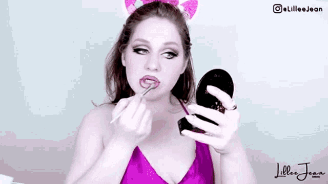 a woman wearing bunny ears is applying lipstick in front of a mirror .