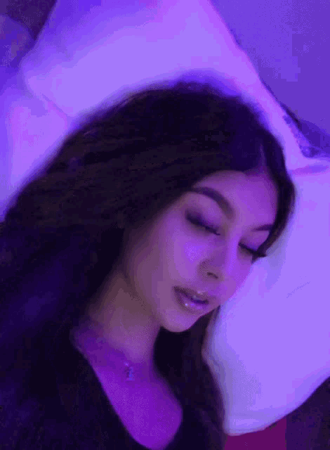 a woman is laying on a bed with purple lights behind her and a white pillow .