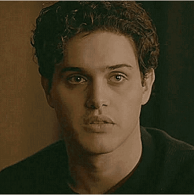 a close up of a man 's face with curly hair and a black shirt .