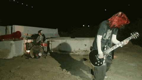 a man with red hair is playing a guitar in front of a drummer