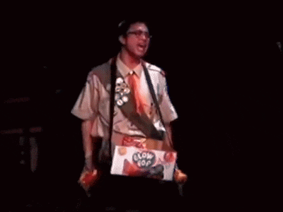 a man in a suit and tie is standing on a stage with a box of pop corn .