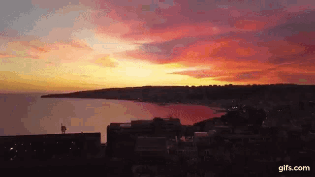 an aerial view of a sunset over a body of water with buildings in the foreground .