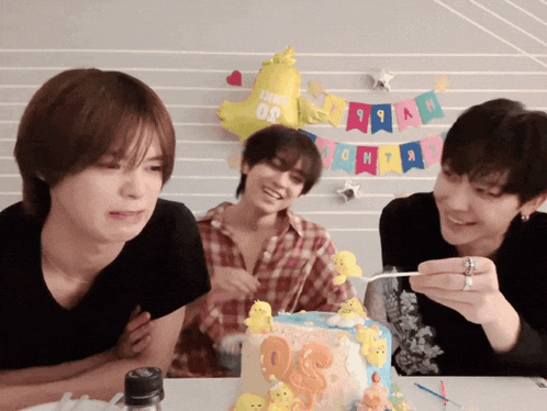 a group of young men are sitting around a birthday cake