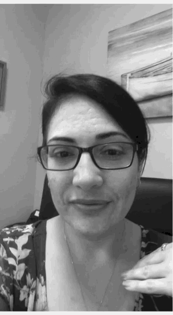a woman wearing glasses and a floral shirt is smiling in a black and white photo