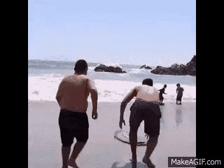 two men are standing on a beach with a surfboard in their hand .