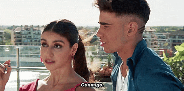 a man and a woman are standing on a balcony and the woman is saying conmigo