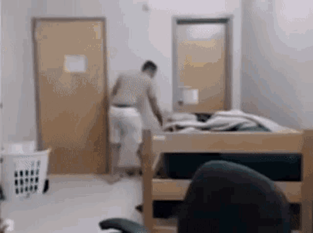 a man is standing in a bedroom next to a bed and a laundry basket .