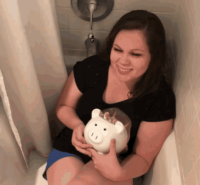 a woman sits in a bathtub holding a piggy bank with coins in it