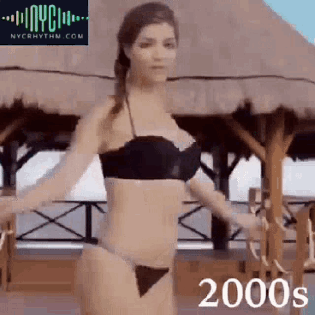 a woman in a bikini is dancing in front of a thatched hut ..