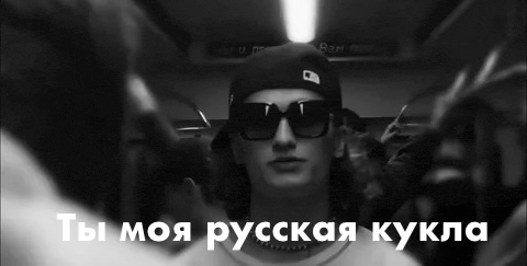 a black and white photo of a man wearing sunglasses and a hat with russian writing on it .
