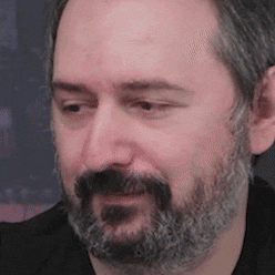 a man with a beard and mustache is wearing a black shirt and looking at the camera .