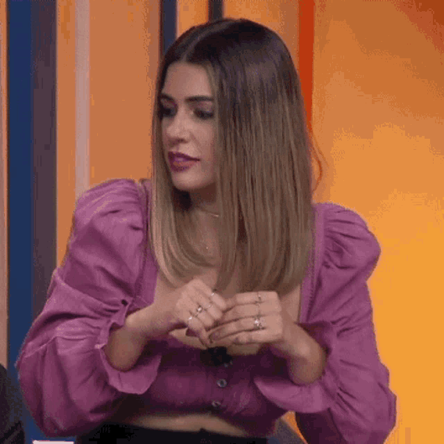a woman wearing a purple crop top and a black skirt is sitting in front of a wall .