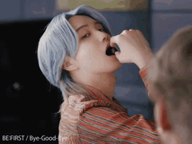 a man with blue hair and a striped shirt says be first