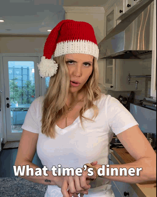 a woman wearing a santa hat says what time 's dinner in the kitchen