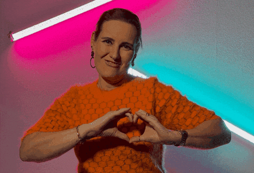 a woman in an orange shirt is making a heart with her hands
