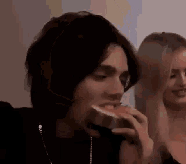 a man is eating a slice of watermelon with a woman standing behind him .