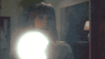 a woman is looking at herself in a mirror with a light shining on her face