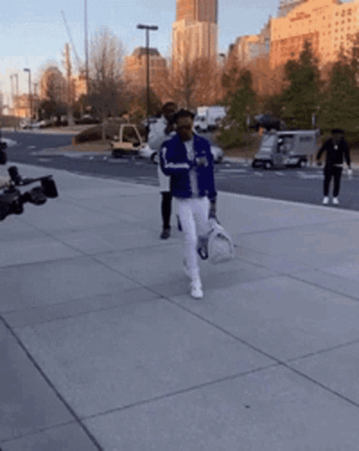 a man in a blue jacket and white pants walking down a sidewalk