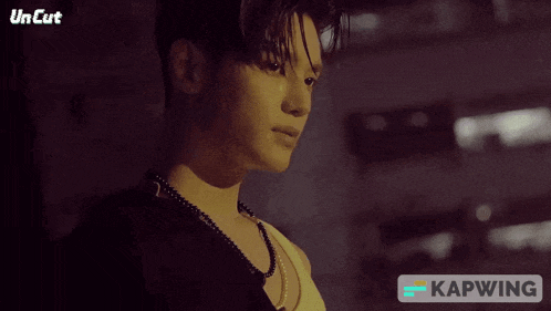a man wearing a necklace and a white tank top with the word kapwing on the bottom